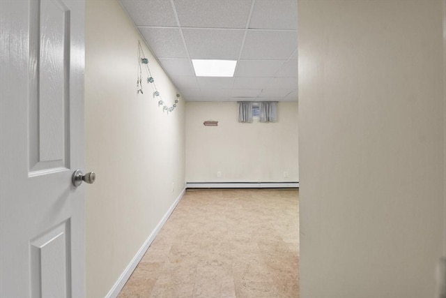 basement featuring a paneled ceiling and a baseboard heating unit