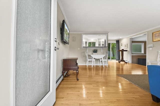 interior space with a baseboard heating unit, ornamental molding, and light hardwood / wood-style floors