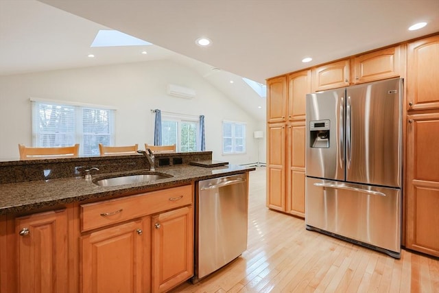 kitchen featuring a wall mounted air conditioner, dark stone counters, stainless steel appliances, lofted ceiling with skylight, and sink