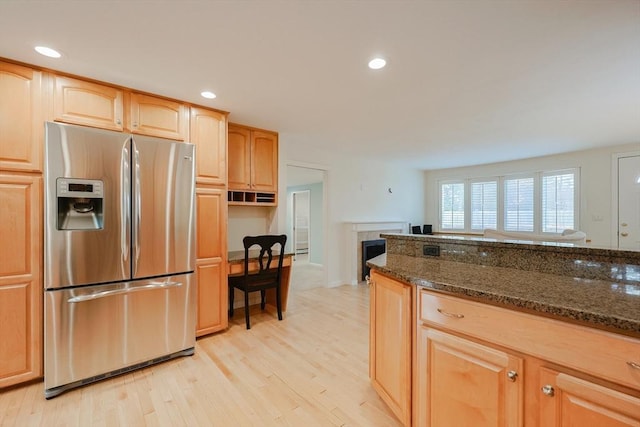 kitchen featuring stainless steel fridge with ice dispenser, light brown cabinets, light hardwood / wood-style floors, and dark stone counters