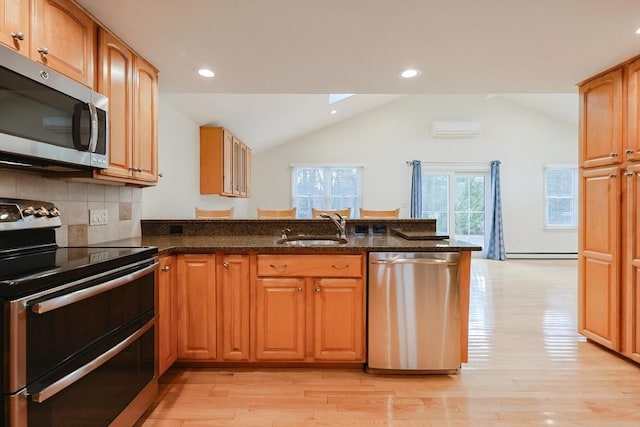 kitchen with kitchen peninsula, stainless steel appliances, vaulted ceiling, sink, and dark stone countertops