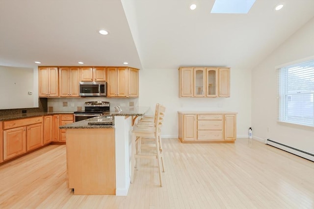 kitchen with a kitchen bar, light wood-type flooring, stainless steel appliances, lofted ceiling with skylight, and dark stone countertops