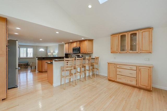 kitchen with kitchen peninsula, a breakfast bar, stainless steel appliances, high vaulted ceiling, and light hardwood / wood-style flooring