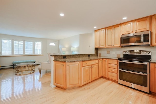 kitchen featuring light brown cabinets, kitchen peninsula, dark stone counters, appliances with stainless steel finishes, and light wood-type flooring