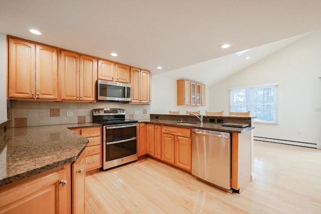 kitchen featuring stainless steel appliances, a baseboard heating unit, kitchen peninsula, dark stone countertops, and vaulted ceiling with skylight