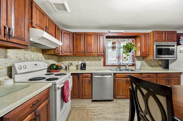 kitchen featuring stainless steel appliances, a sink, under cabinet range hood, decorative backsplash, and light countertops