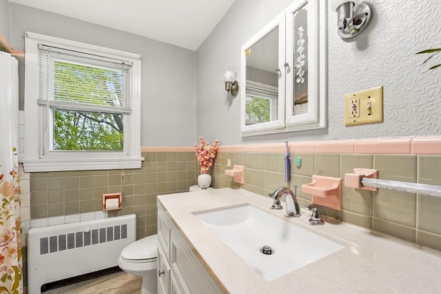 bathroom featuring radiator, toilet, vanity, tile walls, and wainscoting
