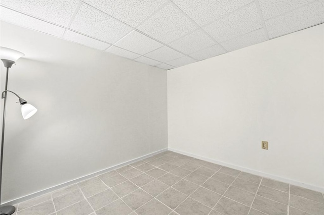 empty room featuring a paneled ceiling, baseboards, and light tile patterned flooring