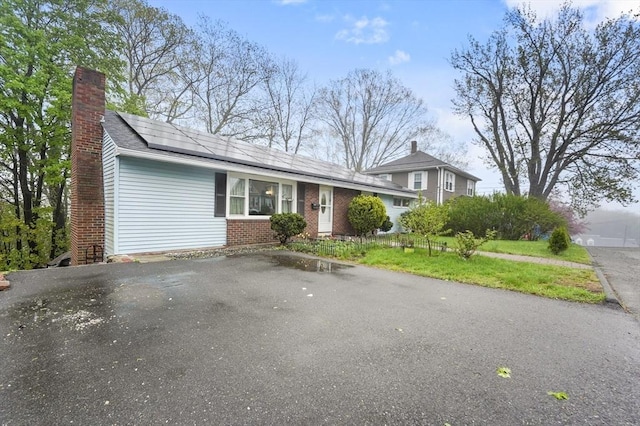 split level home with solar panels, brick siding, a chimney, a front yard, and asphalt driveway