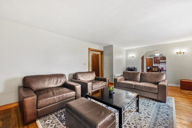 living area with arched walkways, light wood finished floors, and baseboards