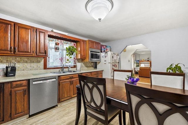 kitchen featuring stainless steel appliances, a sink, arched walkways, decorative backsplash, and light countertops