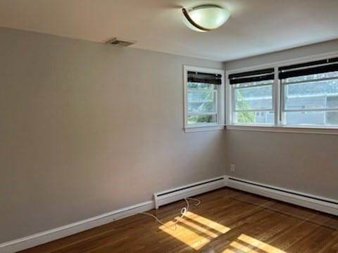 spare room featuring a baseboard radiator and dark wood-type flooring