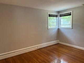 empty room with hardwood / wood-style flooring and a baseboard heating unit