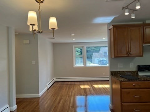 kitchen with dark stone countertops, decorative light fixtures, a baseboard heating unit, and dark hardwood / wood-style flooring