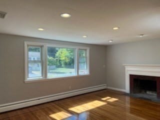 unfurnished living room featuring wood-type flooring and a baseboard heating unit