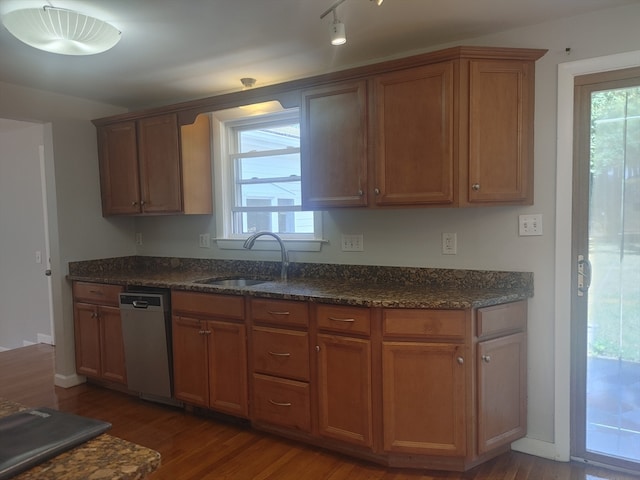 kitchen with dark wood-type flooring, dark stone countertops, dishwashing machine, and sink