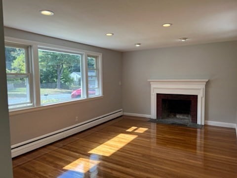 unfurnished living room with wood-type flooring and a baseboard radiator