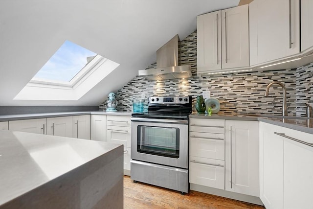 kitchen with vaulted ceiling with skylight, exhaust hood, backsplash, white cabinetry, and stainless steel range with electric stovetop