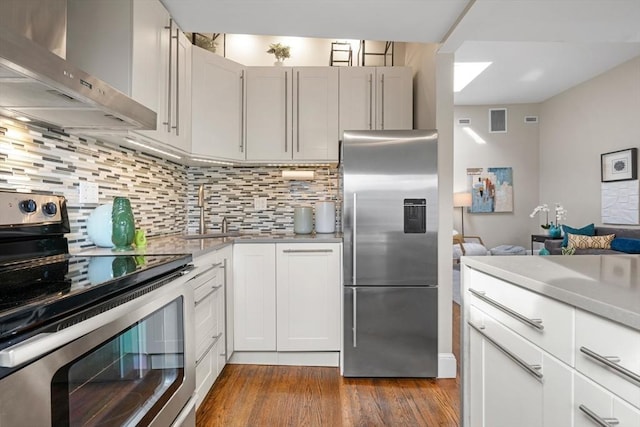 kitchen featuring white cabinets, stainless steel appliances, wall chimney exhaust hood, and tasteful backsplash