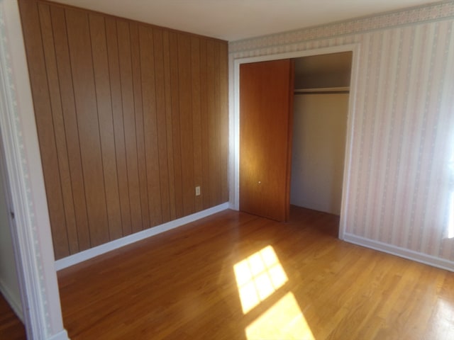 unfurnished bedroom featuring light hardwood / wood-style flooring, wooden walls, and a closet