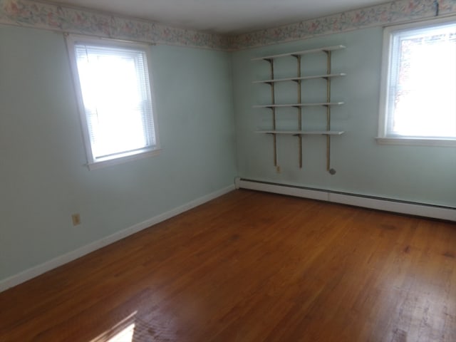 spare room featuring wood-type flooring, a healthy amount of sunlight, and a baseboard heating unit