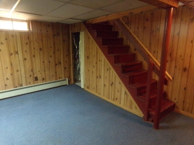 basement featuring wooden walls, a drop ceiling, carpet flooring, and a baseboard heating unit