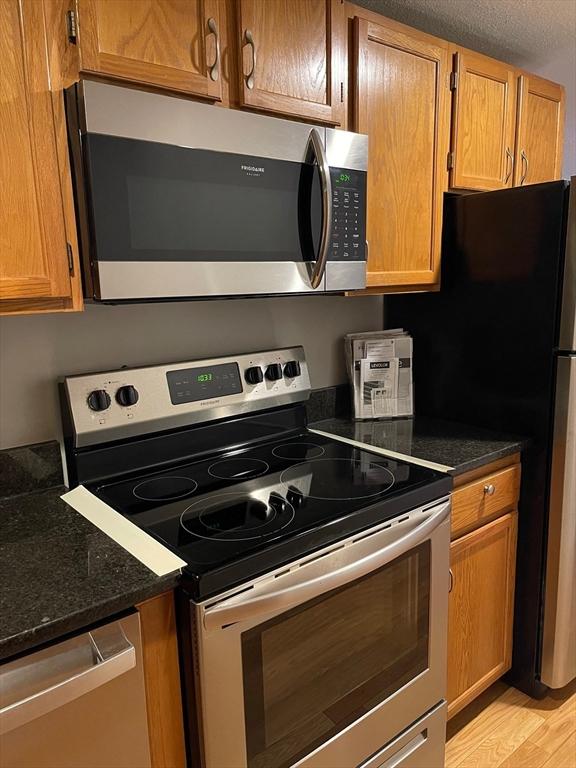 kitchen featuring light wood-type flooring, dark stone counters, a textured ceiling, and appliances with stainless steel finishes