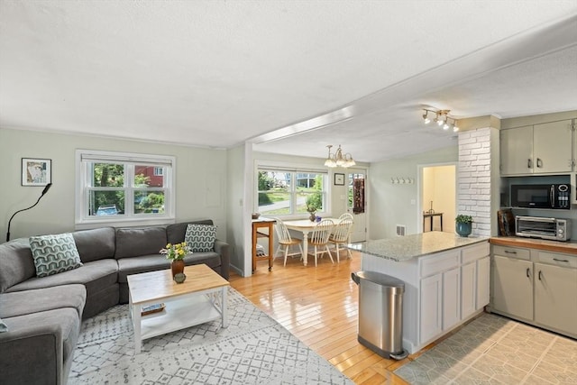 interior space featuring hanging light fixtures, light stone counters, a notable chandelier, kitchen peninsula, and light hardwood / wood-style floors