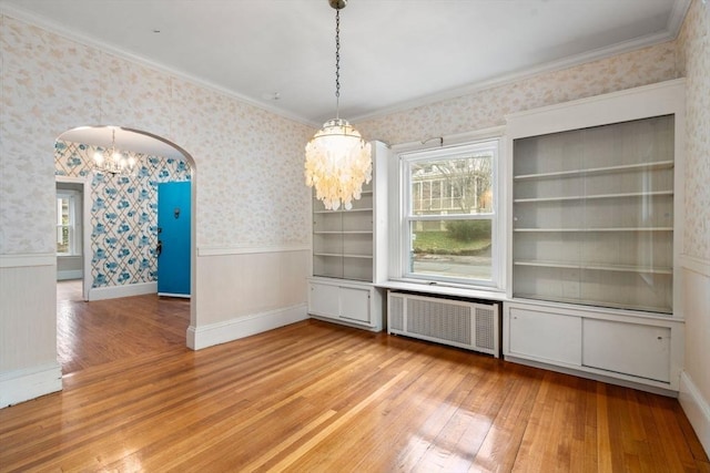 unfurnished dining area with wallpapered walls, arched walkways, radiator, a wainscoted wall, and light wood-type flooring