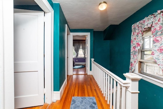 hall featuring a textured ceiling, baseboards, wood finished floors, and a wealth of natural light
