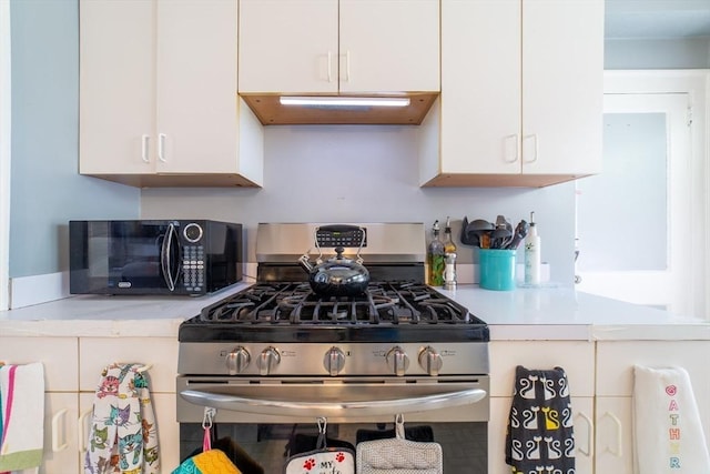 kitchen featuring white cabinets, black microwave, stainless steel range with gas stovetop, light countertops, and under cabinet range hood