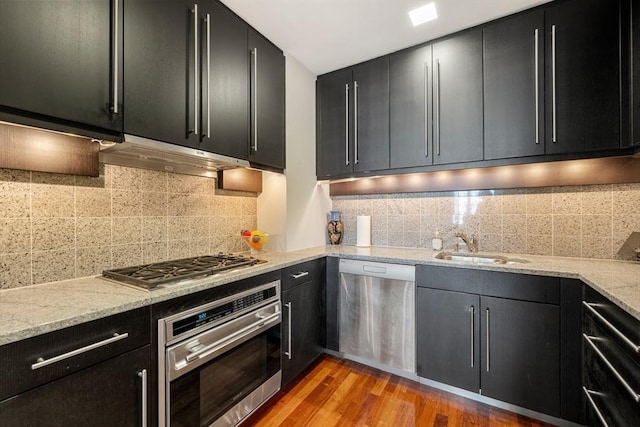 kitchen with light stone countertops, sink, stainless steel appliances, light hardwood / wood-style flooring, and decorative backsplash