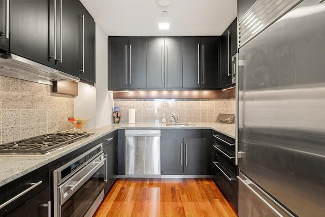 kitchen featuring appliances with stainless steel finishes, light wood-type flooring, tasteful backsplash, and light stone counters