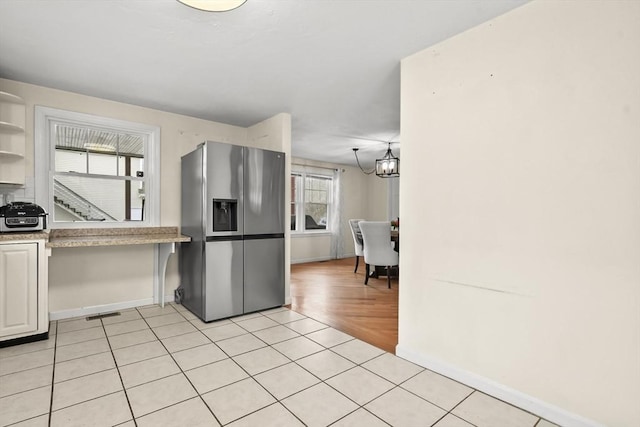 kitchen with stainless steel refrigerator with ice dispenser, open shelves, light countertops, light tile patterned floors, and a chandelier