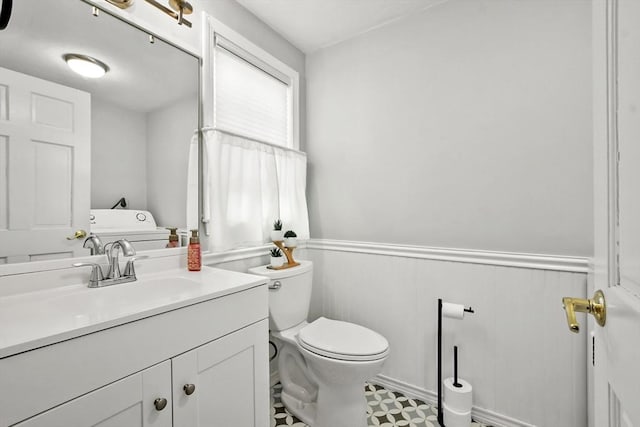 half bathroom featuring vanity, toilet, and wainscoting