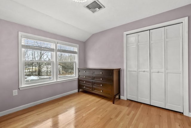 unfurnished bedroom featuring visible vents, a closet, light wood finished floors, baseboards, and vaulted ceiling