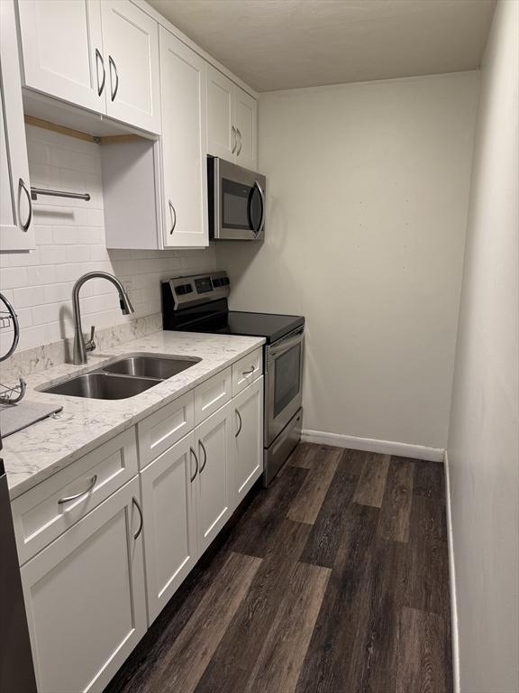 kitchen with sink, white cabinetry, light stone countertops, appliances with stainless steel finishes, and dark wood-type flooring