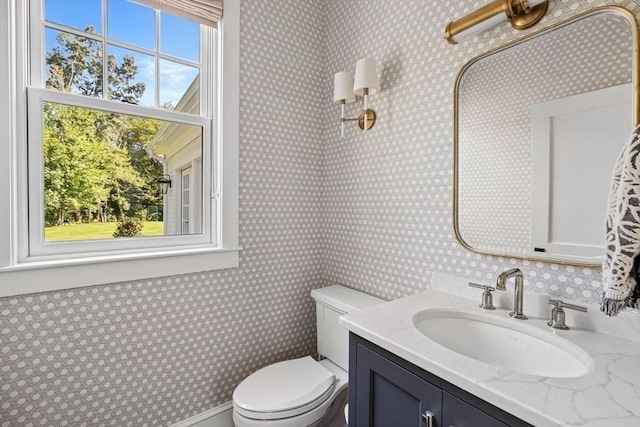 half bath featuring vanity, wallpapered walls, and toilet