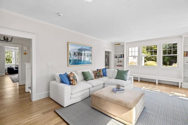 living room with light wood-style floors, ornamental molding, and built in shelves