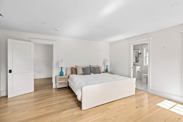 bedroom with connected bathroom, baseboards, and light wood-style flooring