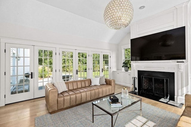 living room with vaulted ceiling, a fireplace with flush hearth, french doors, and light wood-style flooring