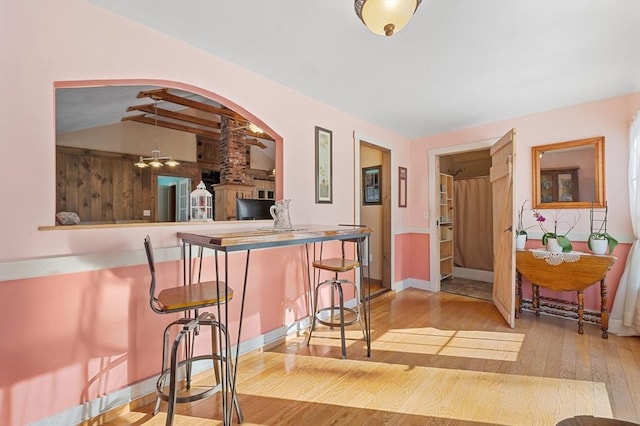 interior space featuring a kitchen bar, hardwood / wood-style flooring, arched walkways, baseboards, and vaulted ceiling with beams