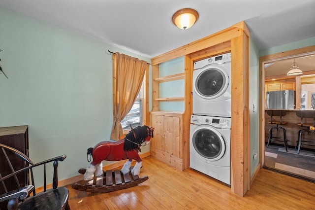 washroom with light wood-type flooring, baseboards, stacked washer and clothes dryer, and laundry area