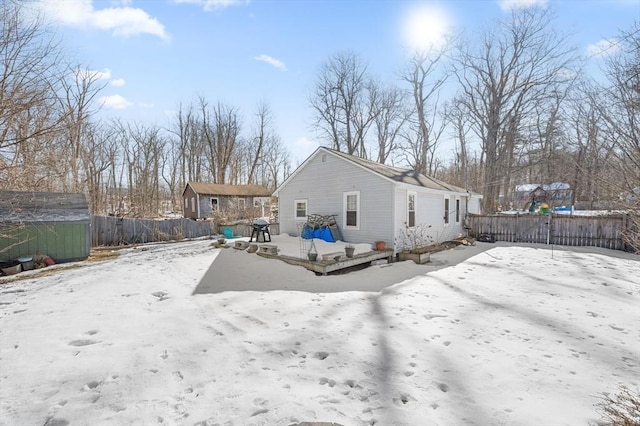 snow covered back of property with a fenced backyard and a wooden deck