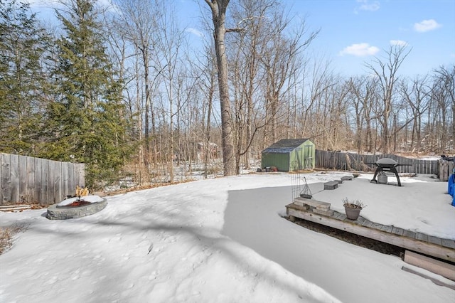 snowy yard featuring an outdoor structure, a storage unit, a fenced backyard, and a fire pit