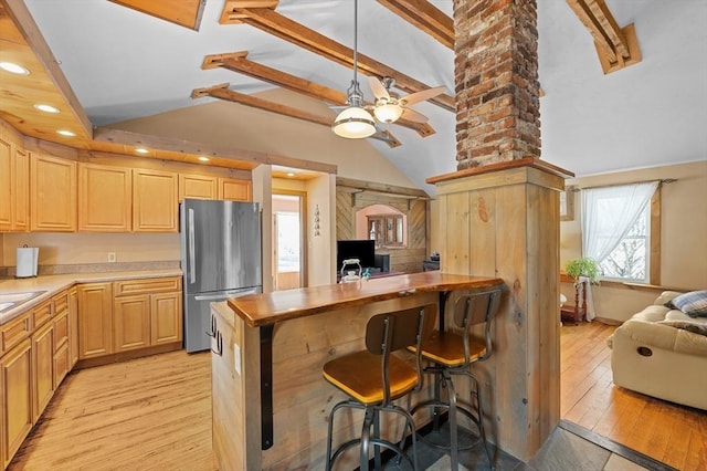 kitchen featuring beamed ceiling, light wood-style flooring, light brown cabinets, and freestanding refrigerator