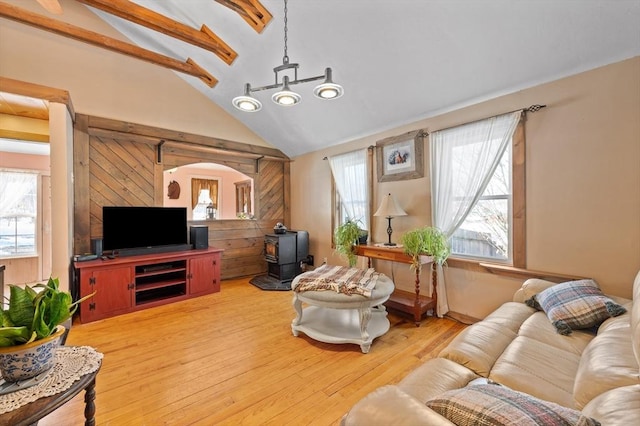 living room featuring a wood stove, vaulted ceiling with beams, light wood-style floors, and plenty of natural light