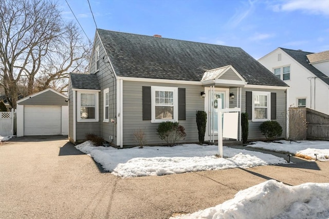 view of front of property featuring driveway, roof with shingles, a detached garage, and an outdoor structure