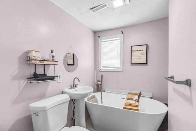 bathroom with a tub to relax in, toilet, and a textured ceiling