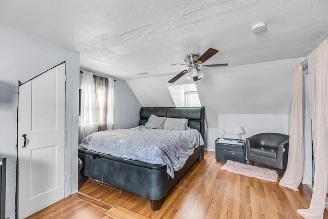 bedroom with vaulted ceiling, ceiling fan, a textured ceiling, and light hardwood / wood-style flooring